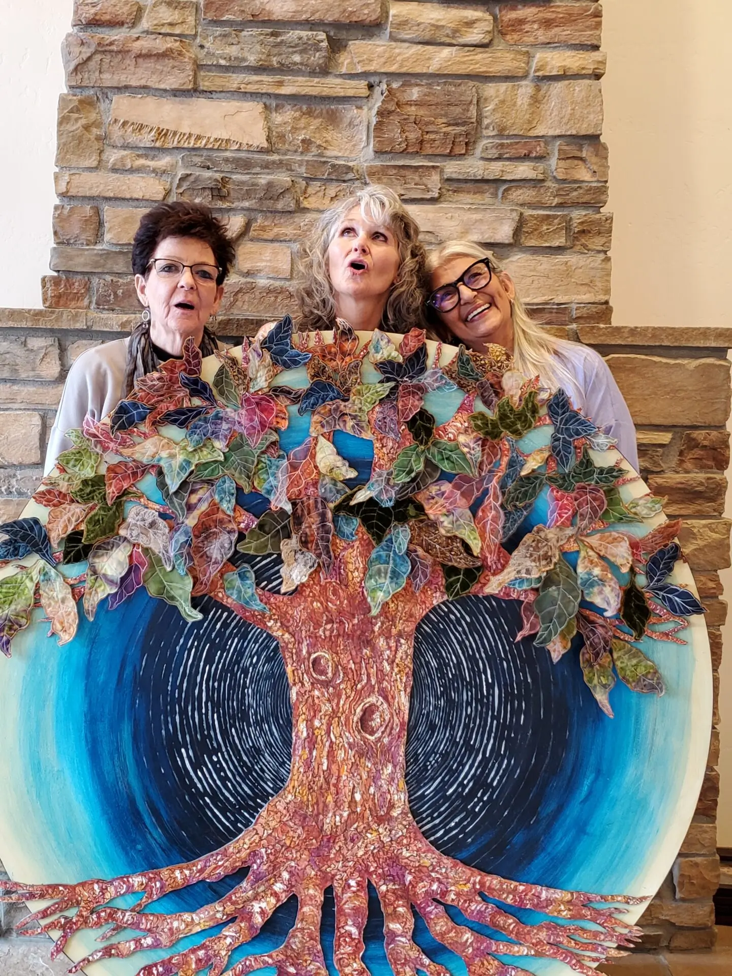 Three women are posing with a large painting.