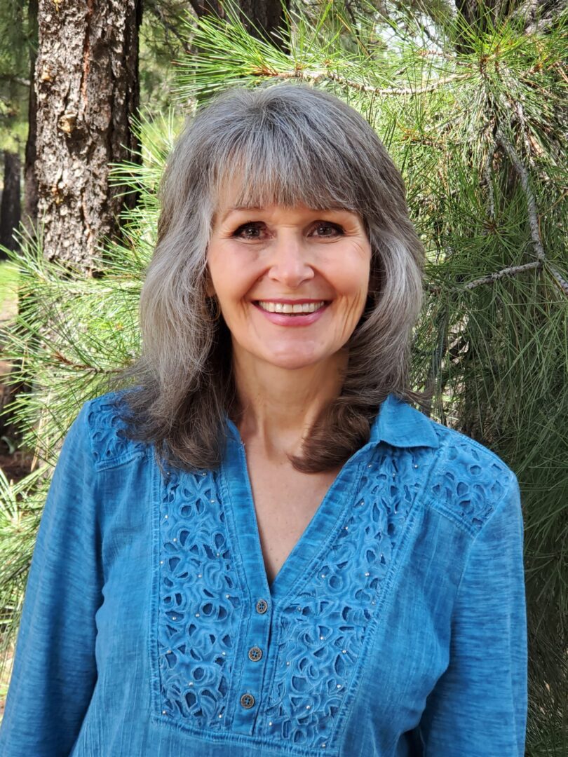 A woman with grey hair and blue shirt smiling.